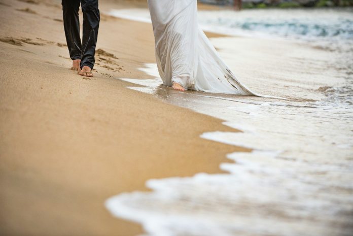 Photo by Isaac Quesada man in white dress shirt and blue denim jeans walking on beach during daytime